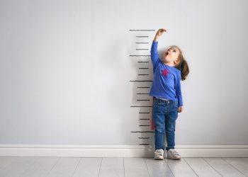 Little child is playing superhero. Kid is measuring the growth on the background of wall. Girl power concept.